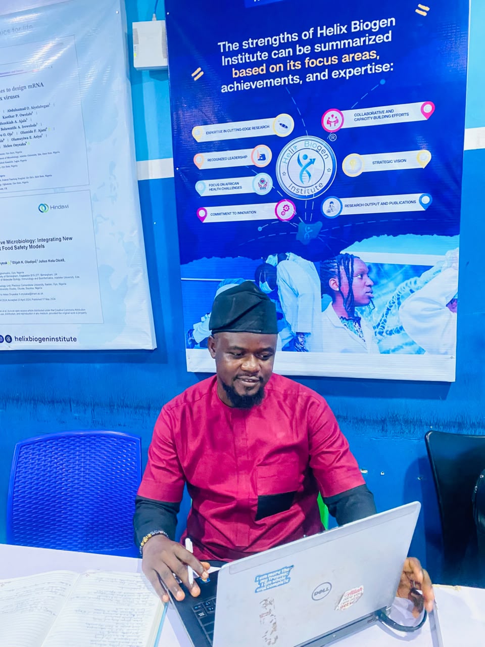 Toheeb Ayodeji Sodiq working at a research desk with scientific posters behind him